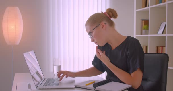 Retrato de close-up de jovem atraente mulher de negócios caucasiana em óculos usando laptop ter telefonema tomando notas no escritório dentro de casa — Vídeo de Stock