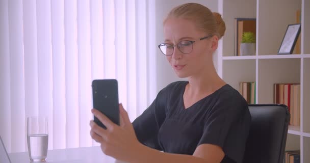 Closeup portrét mladé přitažlivé kavkazské ženy v brýlích s videotelefonem v kanceláři v interiérech — Stock video
