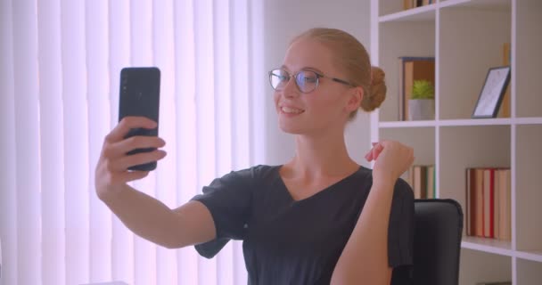 Κοντινό πλάνο του νεαρού ελκυστική Καυκάσιος επιχειρηματίας σε γυαλιά παίρνοντας selfie των στο τηλέφωνο χαμογελαστά ευτυχισμένα στο γραφείο σε εσωτερικούς χώρους — Αρχείο Βίντεο
