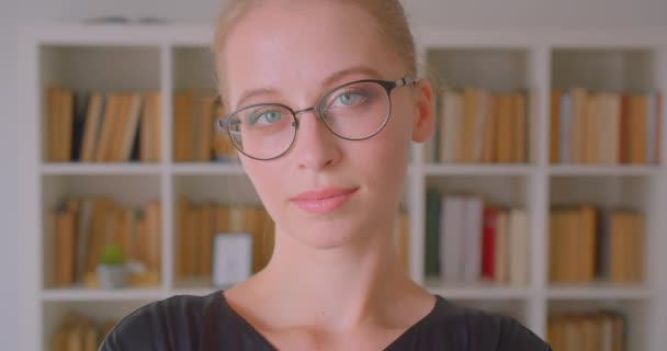 Closeup portrait of young attractive caucasian female student in glasses looking at camera in library indoors — Stock video