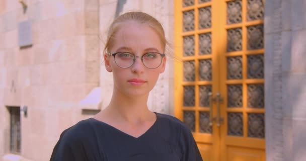 Zbliżenie Portret młodej atrakcyjnej kobiety kaukaski w okularach patrząc na kamery na zewnątrz na ulicy — Wideo stockowe
