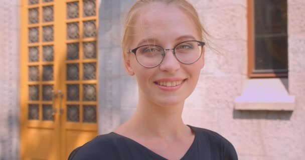 Primer plano retrato de joven atractiva mujer caucásica en gafas mirando a la cámara sonriendo alegremente al aire libre en la calle en la ciudad — Vídeos de Stock