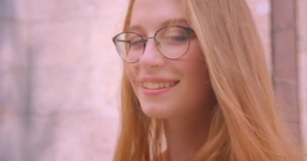 Retrato de close-up de jovem mulher branca atraente com cabelos longos em óculos olhando para a câmera sorrindo alegremente com vento soprando ao ar livre — Vídeo de Stock