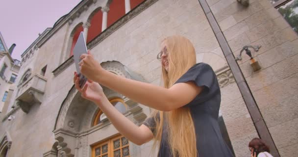 Zbliżenie Portret młodej kobiety z długimi włosami w okularach o połączenie wideo na tablecie machając Hi na zewnątrz na ulicy z wieje wiatr — Wideo stockowe
