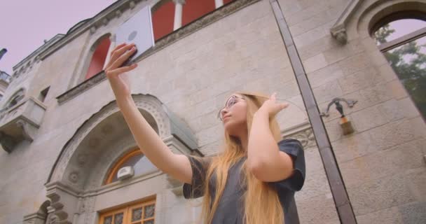 Primo piano ritratto di giovane attraente femmina caucasica con i capelli lunghi in occhiali prendere selfie su tablet all'aperto sulla strada con vento che soffia — Video Stock