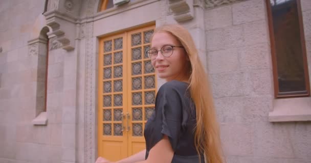 Close-up portret van jonge aantrekkelijke Kaukasische vrouw met lang haar in glazen en jurk houden kick scooter kijken naar camera buitenshuis — Stockvideo