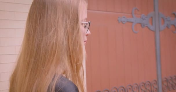 Gros plan portrait de jeune jolie femelle aux cheveux longs dans des lunettes et robe de marche avec coup de pied scooter heureusement à l'extérieur — Video