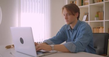 Ofis kapalı kamera bakarak dizüstü bilgisayar kullanarak genç çekici kafkas işadamıcloseup portre