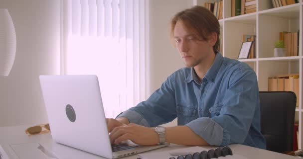 Close-up retrato de jovem bem sucedido atraente homem de negócios caucasiano usando laptop olhando para a câmera no escritório dentro de casa — Vídeo de Stock