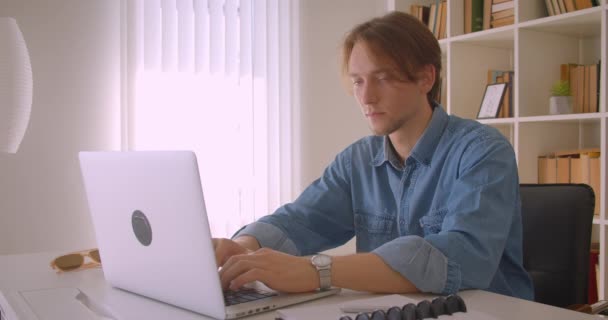 Primo piano ritratto di giovane uomo d'affari caucasico attraente di successo utilizzando computer portatile guardando la fotocamera in ufficio al chiuso — Video Stock