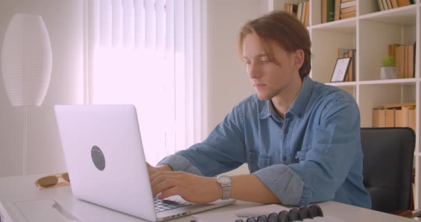 Nahaufnahme Porträt eines jungen attraktiven kaukasischen Geschäftsmannes mit Laptop, der glücklich lächelnd in die Kamera im Büro drinnen blickt — Stockvideo
