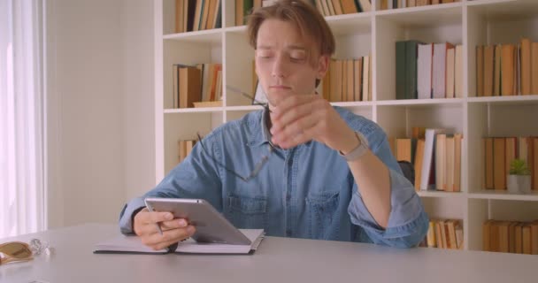 Primer plano retrato de joven atractivo hombre de negocios caucásico en gafas usando tableta en la oficina en interiores — Vídeos de Stock