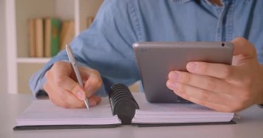 Kapalı kütüphanede notlar alarak tablet kullanarak gözlük çekici kafkas erkek öğrencinin Closeup portre
