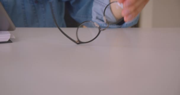 Retrato de primer plano de un estudiante caucásico en gafas usando tabletas tomando notas en la biblioteca en interiores — Vídeos de Stock