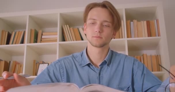 Primer plano retrato de joven atractivo caucásico estudiante masculino en gafas aprendizaje en la biblioteca en interiores — Vídeos de Stock