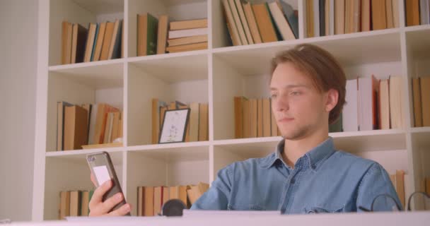 Close-up retrato de jovem atraente homem de negócios caucasiano ter uma chamada de vídeo no telefone no escritório dentro de casa — Vídeo de Stock