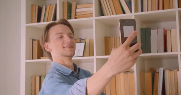 Primer plano retrato de joven guapo caucásico hombre de negocios tomando selfies en el teléfono en la oficina en el interior — Vídeos de Stock