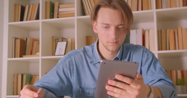 Primer plano retrato de joven atractivo hombre de negocios caucásico usando tableta tomando notas en la oficina en el interior — Vídeos de Stock