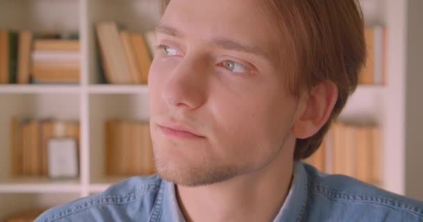 Primer plano retrato de joven guapo caucásico mirando a la cámara en la biblioteca en el interior — Vídeos de Stock