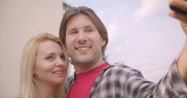 Nahaufnahme Porträt eines erwachsenen attraktiven kaukasischen Paares, das Selfies am Telefon macht und sich glücklich auf dem Balkon des Hauses umarmt