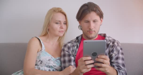 Retrato de close-up de casal adulto atraente caucasiano usando tablet e mostrando tela de croma verde para câmera juntos sentados no sofá dentro de casa — Vídeo de Stock