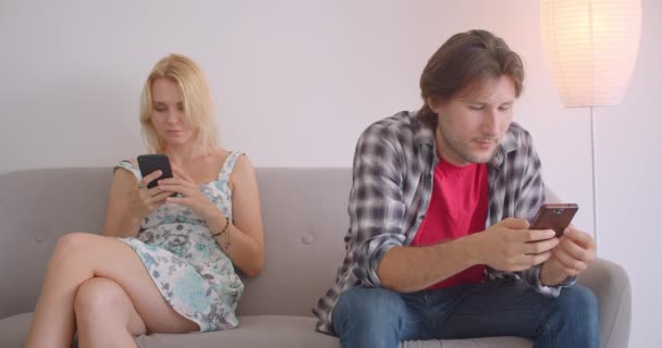 Gros plan portrait d'adulte attrayant couple caucasien à l'aide de téléphones assis sur le canapé à l'intérieur dans l'appartement — Video