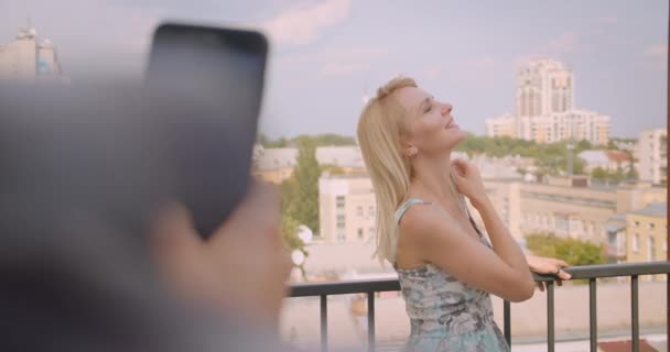 Портрет крупным планом взрослой кавказской женщины, сфотографированной по телефону бойфрендом, стоящим на балконе дома — стоковое видео