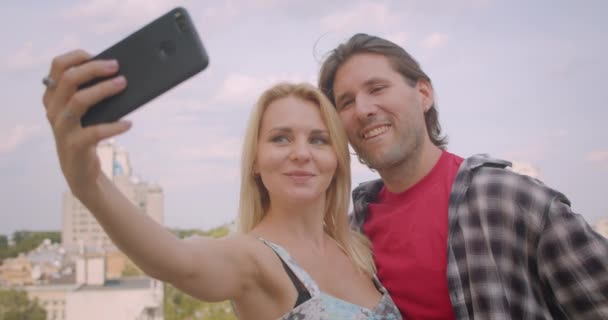 Κοντινό πλάνο του Happy ελκυστικό Καυκάσιος ζευγάρι λαμβάνοντας selfie στο τηλέφωνο αγκάλιασμα στέκεται στο μπαλκόνι του σπιτιού — Αρχείο Βίντεο