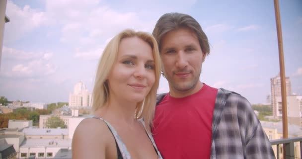 Close-up portret van gelukkige aantrekkelijke Kaukasische paar met video-oproep op telefoon glimlachend vrolijk knuffelen staande op balkon van huis — Stockvideo