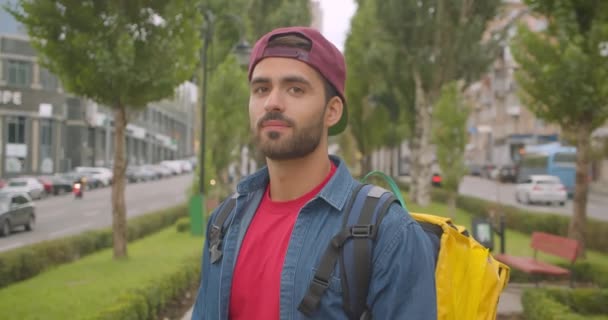 Closeup portréja felnőtt kaukázusi szállítási férfi hátizsák nézi kamera mosolygós vidáman a városban a szabadban — Stock videók