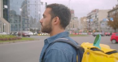 Şehir açık havada karşıdan karşıya geçen sırt çantası ile yetişkin kafkas teslimatçısının closeup yan görünümü
