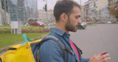 Şehir açık havada telefon crossing sokak kullanarak sırt çantası ile yetişkin kafkas teslimatçı closeup yan görünüm portresi