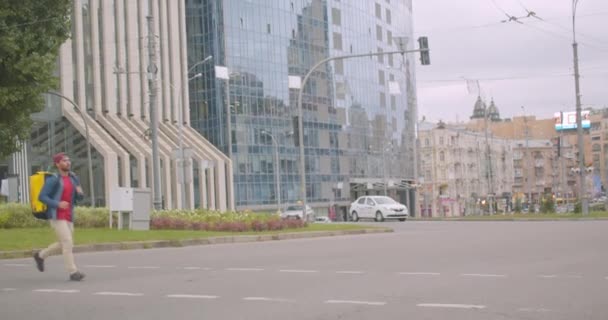 Retrato de adulto caucásico repartidor hombre con mochila corriendo a través de la calle en la ciudad al aire libre — Vídeos de Stock