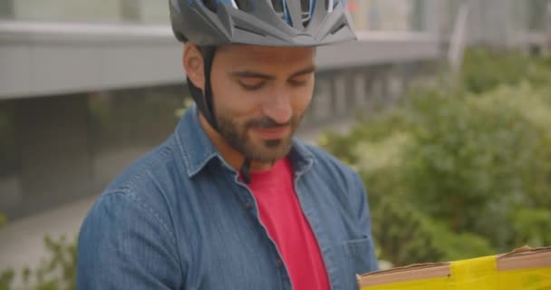 Closeup portrait of bearded caucasian delivery mans hands putting box in backpack to ship in city outdoors with cityscrapers — Stock Video