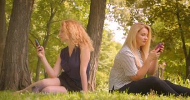 Yeşil park açık havada battaniye üzerinde oturan telefonları kullanarak iki güzel kadın arkadaş Closeup portre