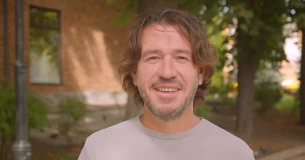 Primer plano retrato de atractivo hombre caucásico mirando a la cámara sonriendo felizmente en la ciudad al aire libre — Vídeos de Stock