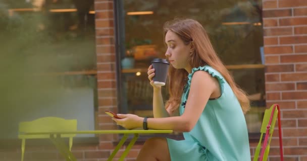 Zbliżenie Portret młodej pięknej kaukaski kobiece picie kawy o telefon siedzi w kawiarni na świeżym powietrzu — Wideo stockowe