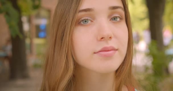 Close-up portret van jonge mooie blanke vrouw kijken naar camera glimlachend vrolijk met flatterend haar staande in Park buitenshuis — Stockvideo