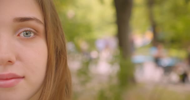 Closeup metade rosto retrato de jovem bonito caucasiano fêmea olhando para a câmera sorrindo feliz de pé no parque ao ar livre — Vídeo de Stock