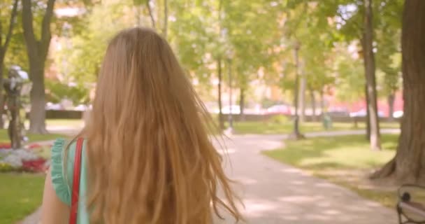 Крупным планом задний вид портрет молодой длинноволосой красивой женщины, идущей поворачиваясь и глядя в камеру с лестными волосами, счастливо улыбающейся в парке . — стоковое видео