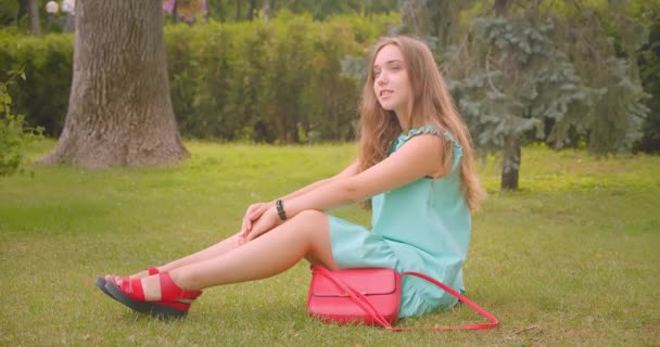 Nahaufnahme Porträt einer jungen langhaarigen schönen Frau, die auf Gras sitzt und im Park im Freien ruht — Stockvideo