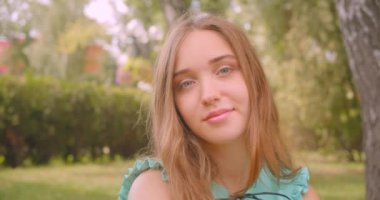 Park açık havada mutlu bir şekilde kameraya bakarak çim üzerinde oturan genç uzun saçlı güzel kadın Closeup düz portre