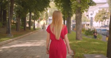 Park açık havada yürüyen kırmızı elbiseli genç sarı uzun saçlı güzel kadın Closeup geri görünümü