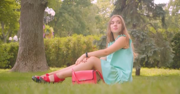 Primer plano retrato de joven de pelo largo hermosa hembra sentada en la hierba descansando felizmente en el parque al aire libre — Vídeo de stock