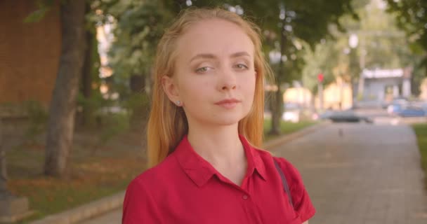 Closeup retrato de jovem bela mulher caucasiana em vestido vermelho olhando para a câmera em pé no parque ao ar livre — Vídeo de Stock