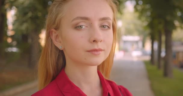 Nahaufnahme Porträt einer jungen schönen kaukasischen Frau im roten Kleid, die glücklich lächelnd in die Kamera blickt, im Park im Freien stehend — Stockvideo