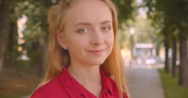 Parkın açık havada neşeyle ayakta gülümseyen kameraya bakan kırmızı elbiseli genç güzel beyaz kadın Closeup portre