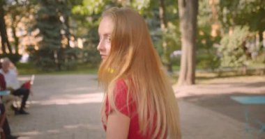 Genç sarı uzun saçlı güzel kadın parketrafında dönen ve kamera açık havada bakarak yürüyüş Closeup geri görünümü portre