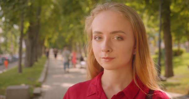 Primer plano retrato de joven linda mujer caucásica en vestido rojo mirando a la cámara sonriendo alegremente de pie en el parque al aire libre — Vídeos de Stock