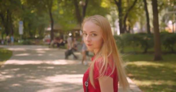 Nahaufnahme Rückseite Porträt der jungen Blondine langhaarige niedliche Frau zu Fuß im Park Drehen und Blick in die Kamera im Freien — Stockvideo